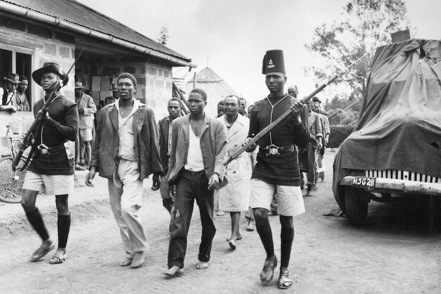 Un groupe d'hommes marchant dans la rue escortés par des soldats