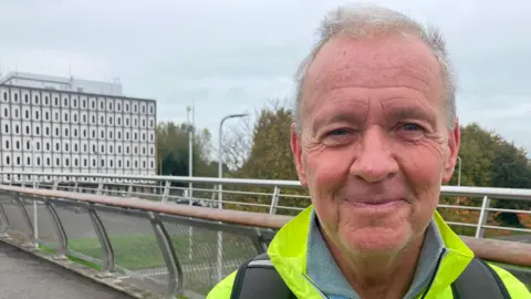 Ronnie Hanna devant Marlborough House, vêtu d'une veste de sécurité.