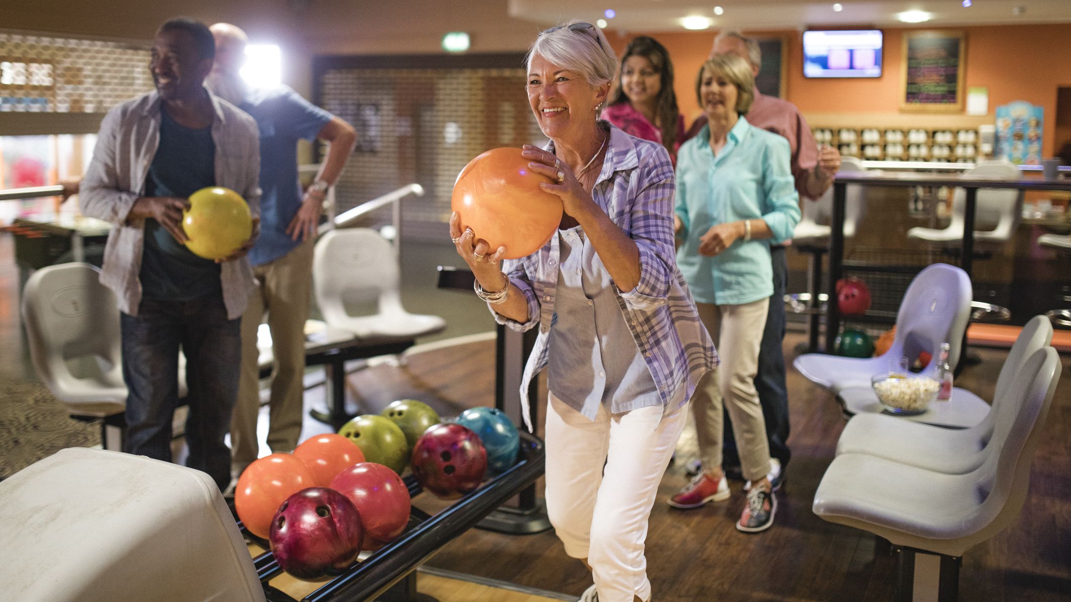 Femme senior tenant une boule de bowling sur le point de jouer dans une allée de bowling.