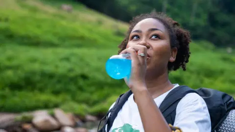 Femme noire buvant une boisson électrolytique après une randonnée