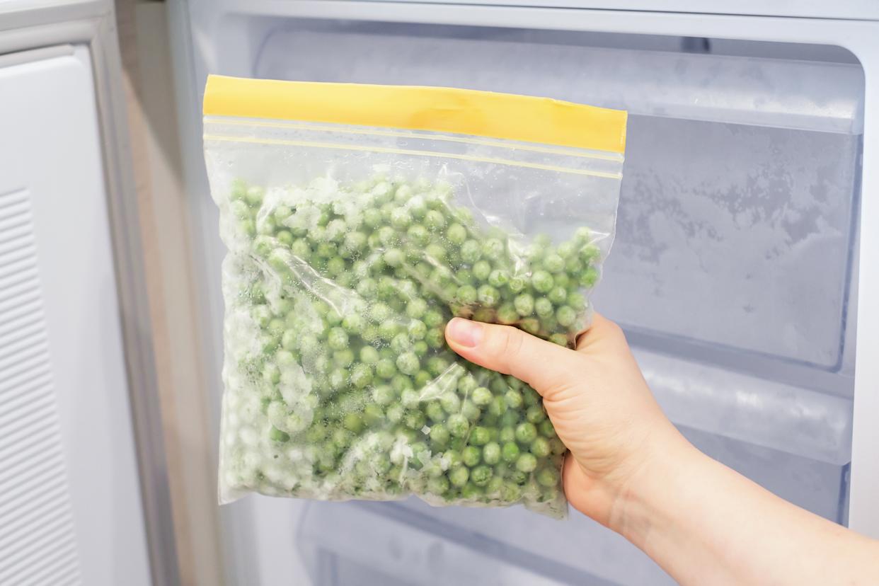 Main féminine tenant un sac zip avec des petits pois verts surgelés