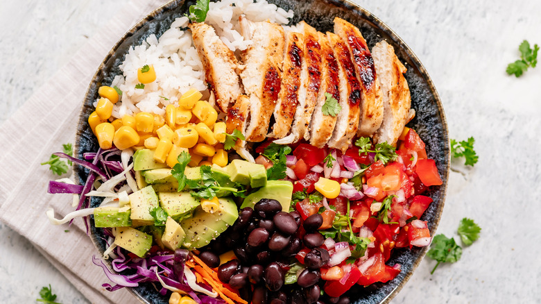 Bol de burrito avec poulet grillé, riz, maïs, haricots noirs, pico de gallo, chou et carottes, et morceaux d'avocat