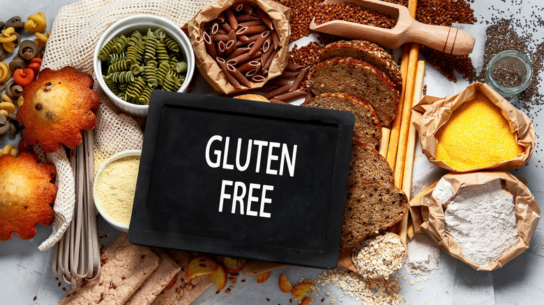 Une pancarte indiquant sans gluten, avec divers ingrédients en arrière-plan, y compris des pâtes crues, du pain et d'autres céréales.