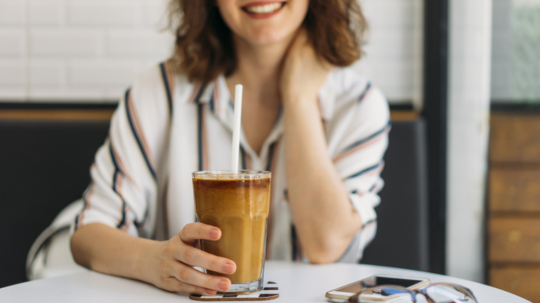 Femme souriante tenant un verre de café glacé