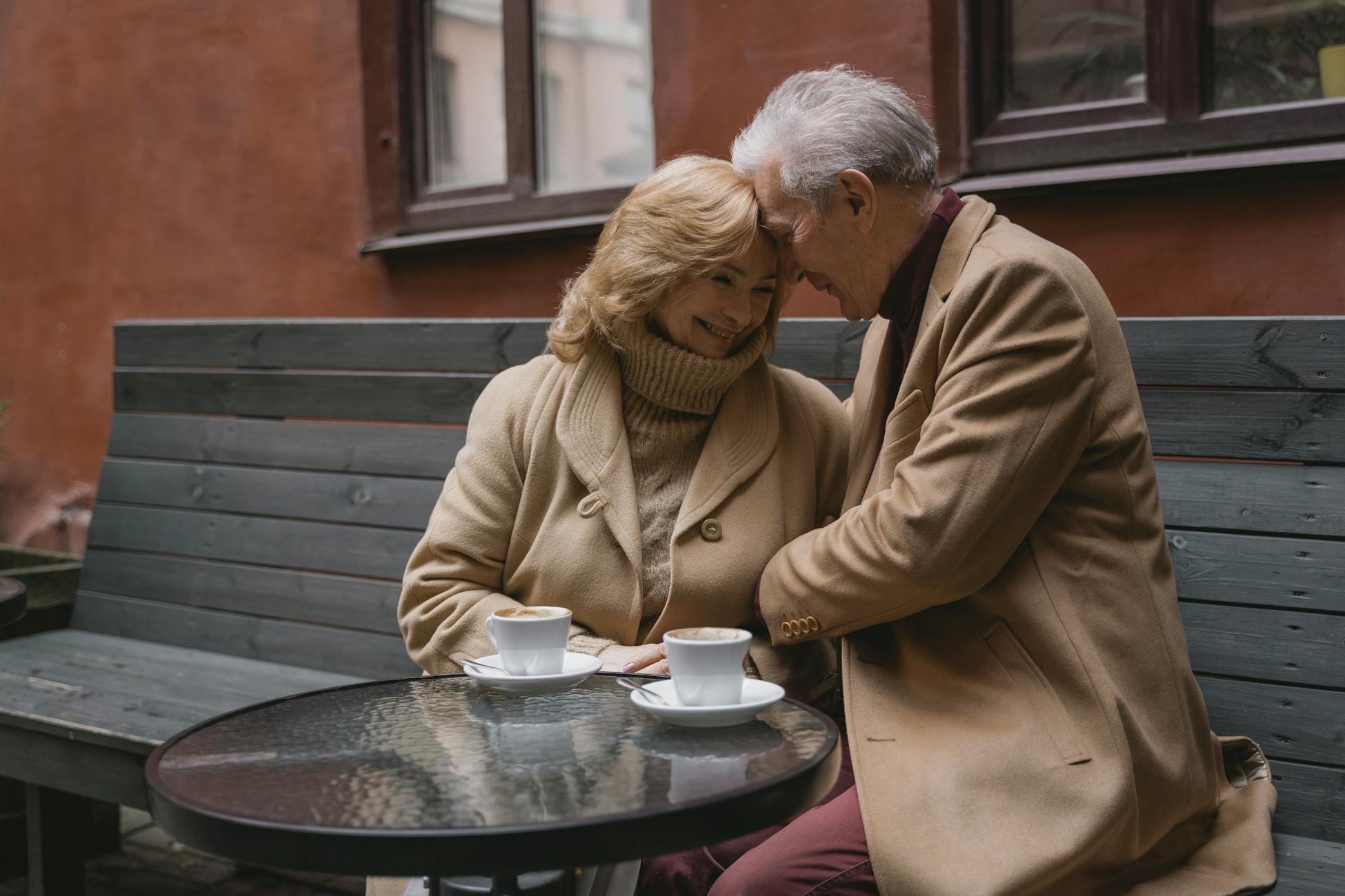 Un couple âgé partage un café sur un banc en plein air, exprimant chaleur et affection.