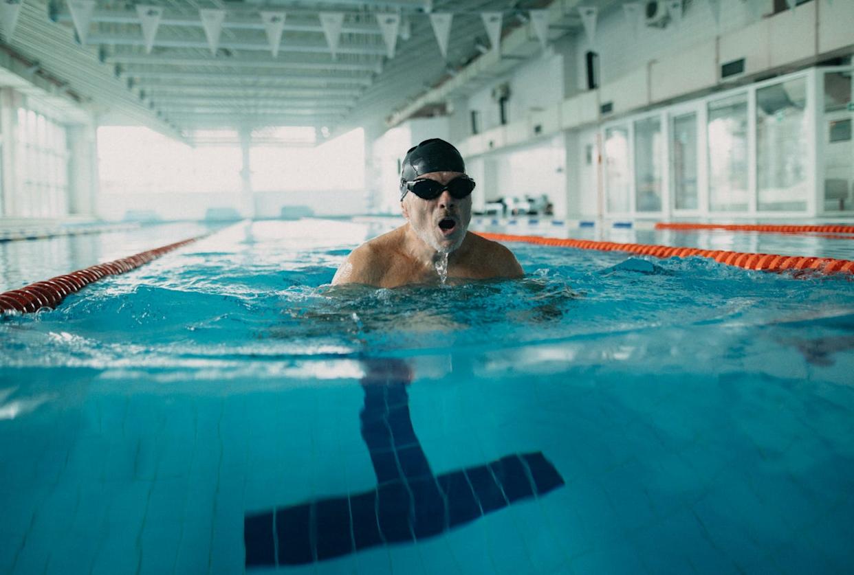 Homme senior actif nageant dans une piscine intérieure.