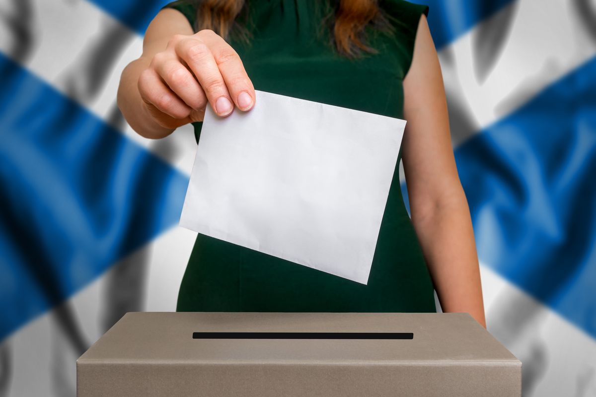 Élection en Écosse - vote dans l'urne. Une main de femme qui insère son vote dans l'urne. Drapeau écossais en arrière-plan.