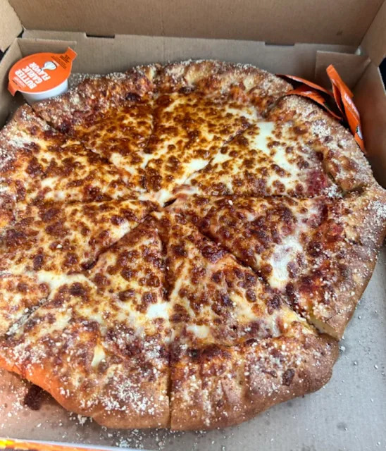 Pizza avec une croûte épaissie et assaisonnée, coupée en huit parts, servie dans une boîte en carton ouverte