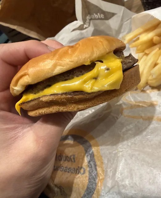 Un cheeseburger avec fromage et boeuf, classique dans les repas de fast-food, avec des frites en arrière-plan