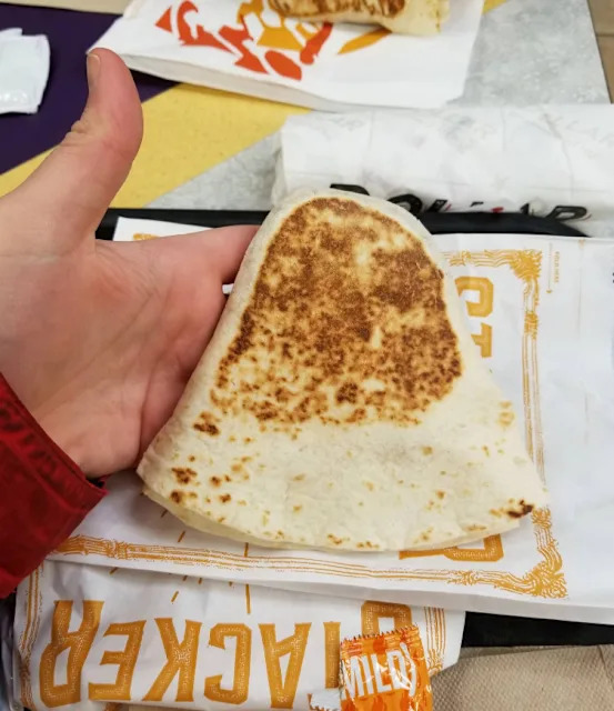 Une quesadilla ou Crunchwrap Supreme de Taco Bell dans une main, avec des paquets de sauce en arrière-plan