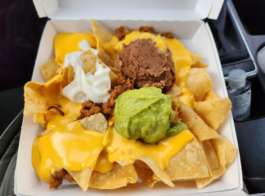 Un contenant à emporter rempli de nachos couverts de fromage fondu, de viande hachée et d'autres garnitures