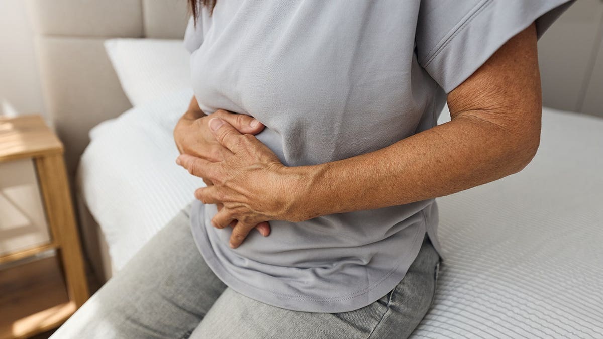 Femme âgée se tenant le ventre, assise sur un canapé à la maison