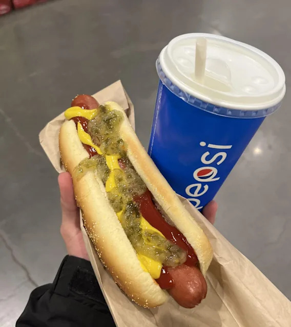 Un hot dog avec ketchup, moutarde et cornichons dans un support en papier, à côté d'un gobelet Pepsi bleu avec une paille