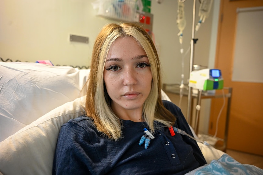 Une jeune femme avec des cheveux châtains et blonds est allongée dans un lit d'hôpital.
