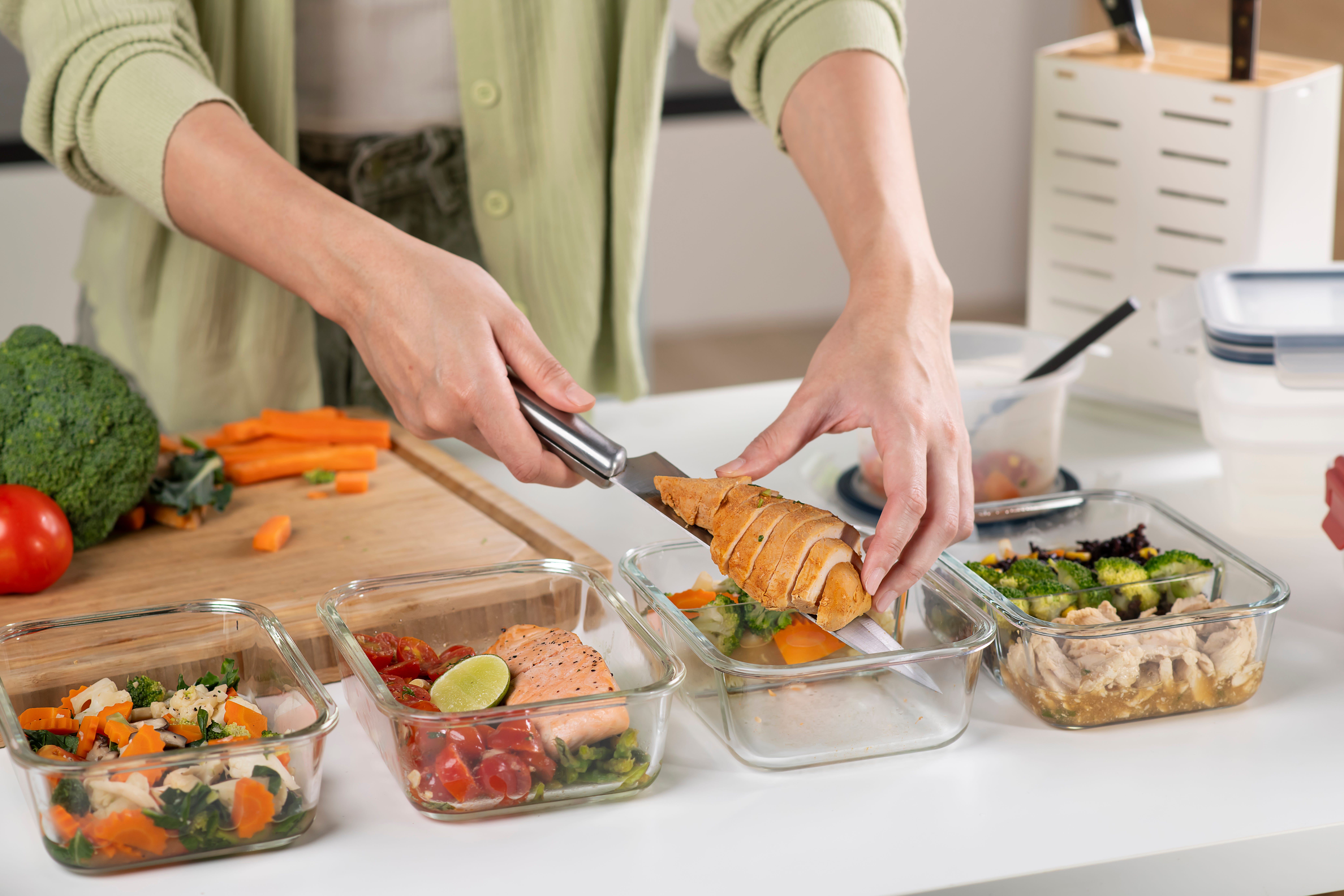 Une femme préparant des repas avec du poulet et des légumes.