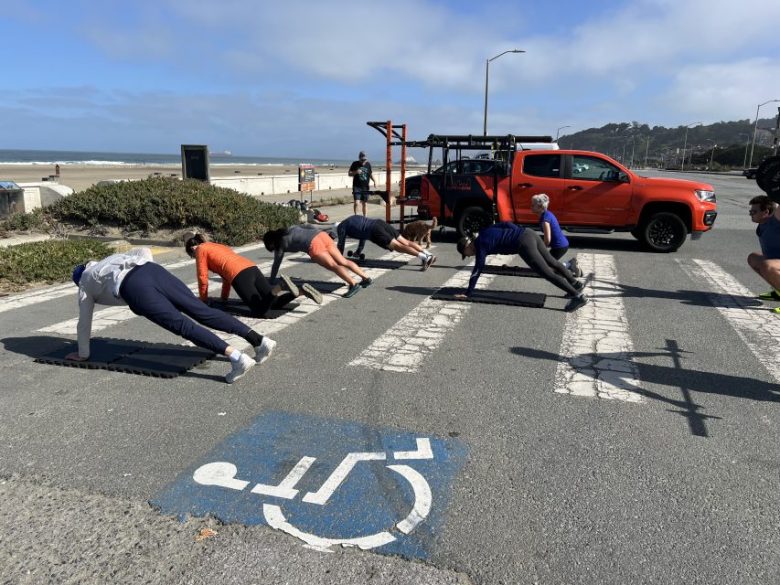 Un groupe de personnes s'exerçant en plein air, avec un camion rouge et un panneau de stationnement accessible visible au premier plan.