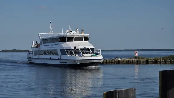 Une ferry blanche arrivant dans un petit port.