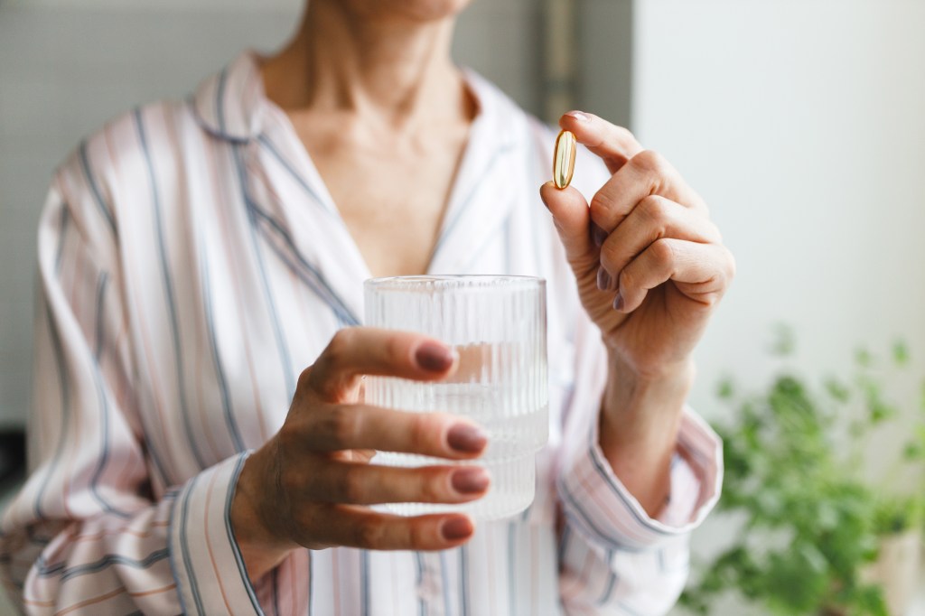 Femme tenant un verre d'eau et une pilule de vitamine D3 ou d'huile de poisson.