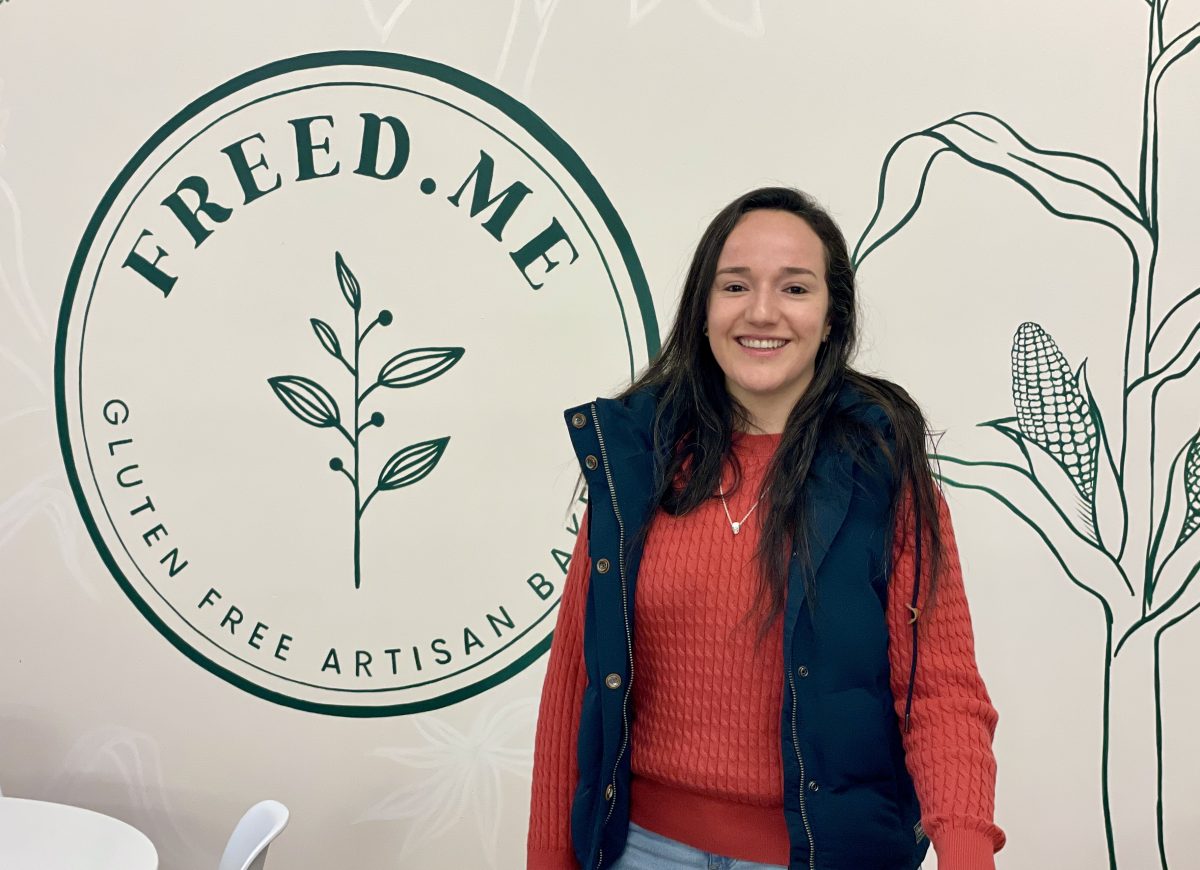 Une jeune femme colombienne porte un pull rouge et un gilet bleu, et se tient devant le logo de Freed.me.
