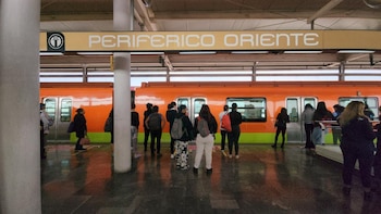 Des passagers attendent sur le quai de la station Periférico Oriente à côté d'un train orange du système de transport