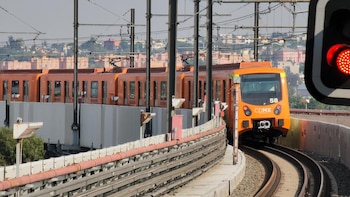 Un train orange avance sur des voies élevées avec un feu ferroviaire rouge en arrière-plan