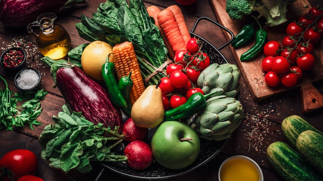 Un bol plein de fruits et légumes sur une table en bois, entouré de plus de fruits, légumes et épices