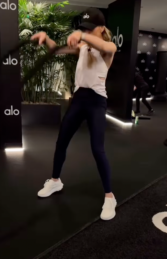 Sarah porte un haut sans manches noir et des leggings bordeaux